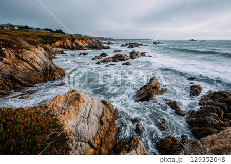 Rugged cliffs meet the turbulent ocean under a cloudy sky 129352048