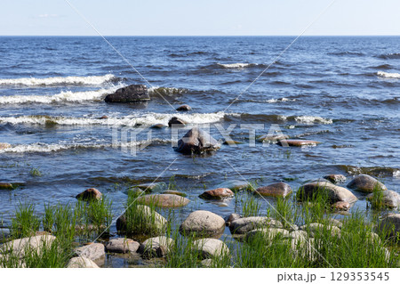 Green grass grows on a rocky coast as lake waves gently break Green grass grows on a rocky coast as lake waves gently break 129353545