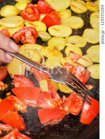 Tomatoes and potatoes cut to pieces grilled on electric grill, hand with fork moving vegetables 129355264