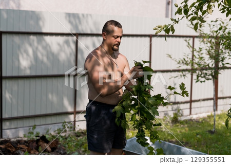 Muscular Man Gardening Outdoors in Shorts, Pruning Grape Vines Near a Metal Fence and Lush Green Trees, Natural Sunlight. 129355551