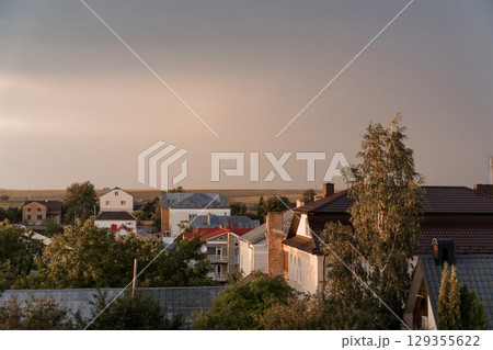 Suburban Sunset View: Brick Houses, Trees, and Landscape with Warm Golden Light - Serene Rural Scene. 129355622