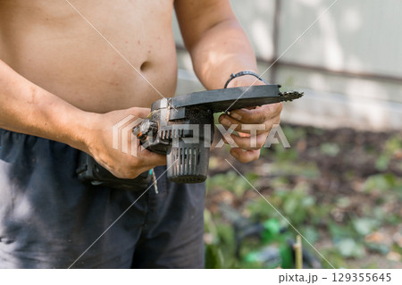 Muscular Torso Holding Black Chainsaw Hand Tool. Gardening, Outdoor Work, Metal Texture, Black Color Scheme, Bare Chest, Summer Yard Maintenance Muscular Torso Holding Black Chainsaw Hand Tool. Gardening, Outdoor Work, Metal Texture, Black Color Scheme, Bare Chest, Summer Yard Maintenance 129355645