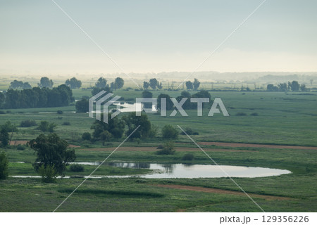 River valley in morning fog, bright sun rays illuminating meadow. Beautiful landscape of river valley in summer 129356226