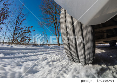 Car navigating through snowy winter road on bright sunny day. A vehicle drives along a snowy road under a clear blue sky, enjoying the winter scenery 129356294