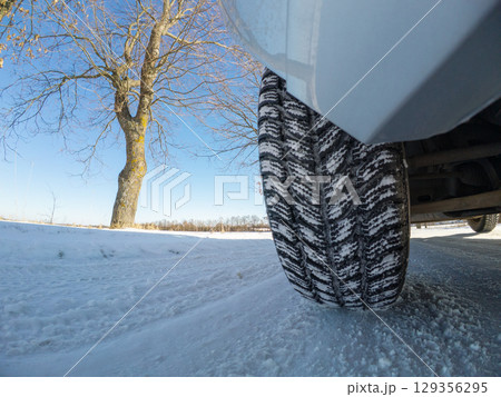 Car tires on snowy winter road. Car with winter tread tires stopped on roadside after a ride on snowy road under clear blue skies, difficult dangerous conditions to drive 129356295