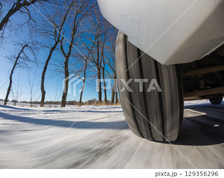 Car navigates snowy winter road under bright sunshine in clear sky. Vehicle drives fast along a snow-covered road on a sunny winter day with blue skies and trees lining the route 129356296