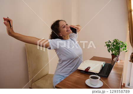 Woman Cheerfully Working from Home With Coffee and Laptop on Desk Woman Cheerfully Working from Home With Coffee and Laptop on Desk 129358789