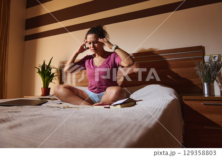 Stressed Young Woman Studying on Bed in a Cozy Home Setting Stressed Young Woman Studying on Bed in a Cozy Home Setting 129358803