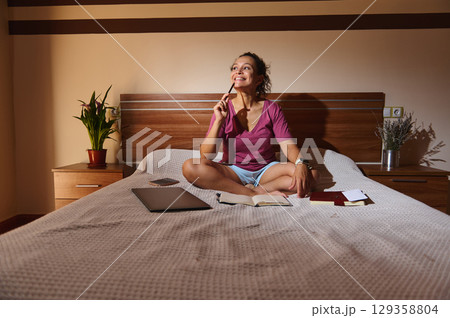 Woman Enjoying Creative Work in a Relaxed Home Bedroom Setting 129358804