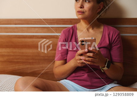 Woman Holding Smartphone Relaxing in a Modern Home Setting 129358809