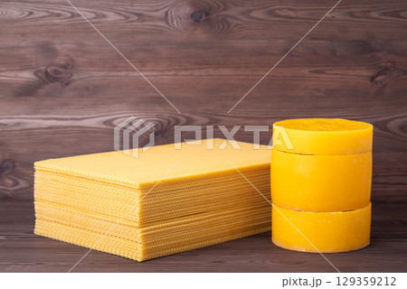 Sheets and cylinders of natural beeswax on wooden background. Yellow wax used for frames in beehive, beekeeping concept 129359212