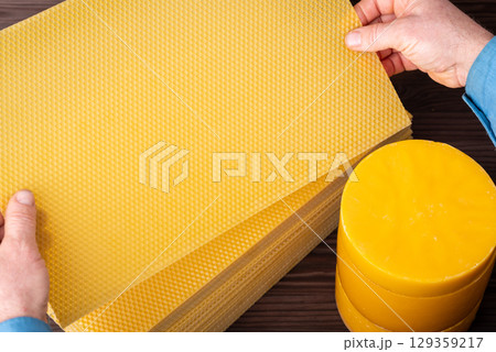 Making new sheets of wax, man looking them through. New sheets of wax made from used one from the hive, stack of wax in cylinders used for making sheets Making new sheets of wax, man looking them through. New sheets of wax made from used one from the hive, stack of wax in cylinders used for making sheets 129359217