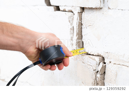 Man measuring crack with a tape measure. Building needs repairing, crack in brick wall 129359292