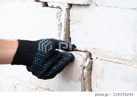 Worker inspecting crack on brick wall before repairing. White brick wall of a building with deep crack Worker inspecting crack on brick wall before repairing. White brick wall of a building with deep crack 129359293