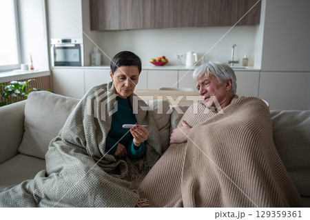 Elderly family sick leave at home. Elderly couple checking temperature with electronic thermometer Elderly family sick leave at home. Elderly couple checking temperature with electronic thermometer 129359361