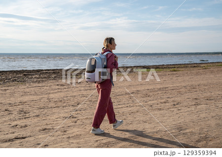Vacation with pet. Calm woman with backpack carrier for cat walking on sandy beach by sea shore 129359394