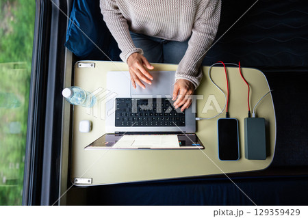 Woman working on laptop while traveling. Computer and smartphone connected to power bank, top view. 129359429