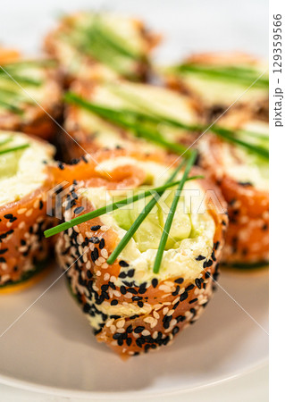 A beautiful arrangement of smoked salmon jumbo cream cheese rolls served on a plate. The rolls are evenly garnished with fresh chives and feature a crunchy sesame seed coating. This dish is a perfect 129359566