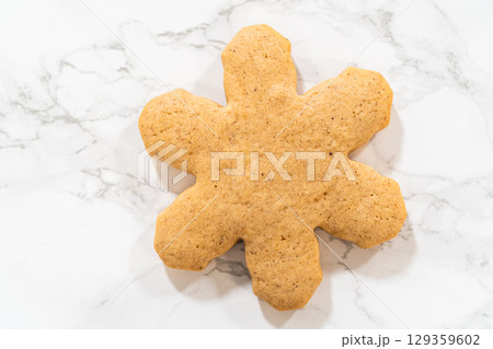 Overhead close-up of a single snowflake-shaped amber gingerbread cookie on a marble countertop, showcasing its detailed design and festive golden color. 129359602