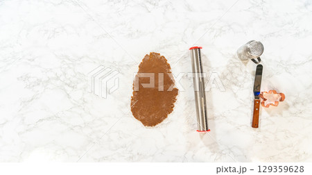 Overhead view of the dough rolling process for Spiced Gingerbread Cookies, showing hands rolling the dough on a marble surface with tools nearby. 129359628