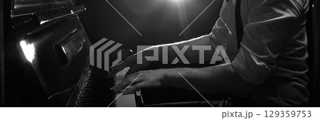 Black and white close-up of pianist hands playing piano under dramatic stage lighting. Banner 129359753