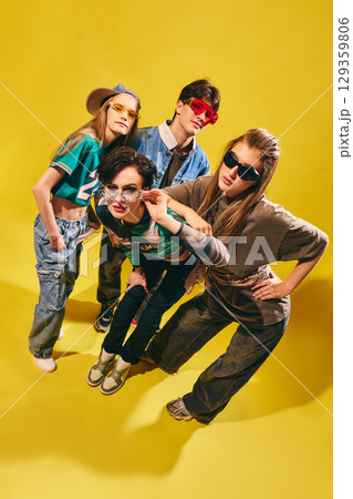 Stylish Gen Z friends in streetwear posing on bright yellow background with confident attitude 129359806