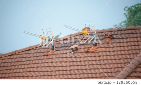 Two television antennas mounted on a tiled rooftop during light rain, France Two television antennas mounted on a tiled rooftop during light rain, France 129360658