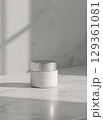 A white cosmetic container with a silver cap sits on a marble surface, with soft shadows creating depth and a serene mood. 129361081