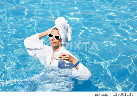 A girl in a white coat swims in a blue pool. Wearing sunglasses and a towel. Epilation of legs, varicose veins. Rest, relaxation on the beach, at the hotel. A woman in freedom. Vacation. High quality 129361139
