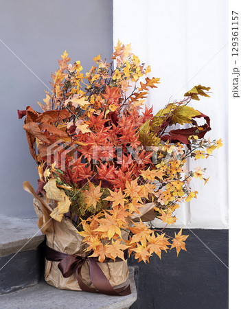 Vibrant autumn arrangement with colorful foliage placed by a minimalist wall Vibrant autumn arrangement with colorful foliage placed by a minimalist wall 129361157
