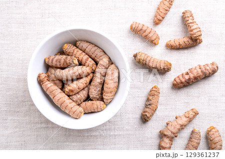 Fresh turmeric rhizomes, in a white bowl, on linen. Underground stems of the turmeric plant Curcuma longa, with bright orange flesh. Used fresh, or dried and ground as turmeric powder. Food photo. 129361237