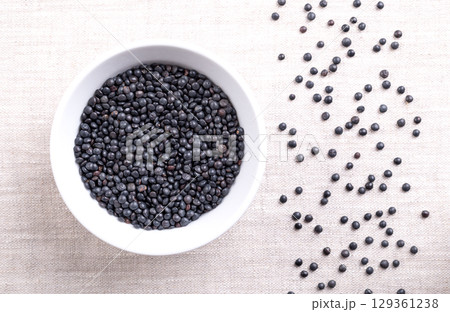 Beluga lentils, black lentils, in a wooden bowl on linen. Dried variety of small lentils, Lens esculenta, also known as caviar lentils. High on fiber and protein, of nutty aroma and of earthy flavor. 129361238