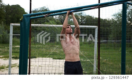 Young muscular sportsman doing pull ups at sports ground. Athletic guy exercising outdoor. Strong sporty man working out at summer nature. Concept of healthy and active lifestyle. Slow motion 129361447