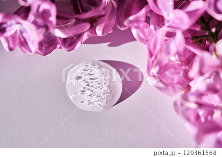 A neat round drop of serum on a white background with bubbles and lilac flowers. A neat round drop of serum on a white background with bubbles and lilac flowers. 129361568