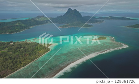 Aerial panorama vibrant coral reef in crystal clear, shallow water of Bora Bora turquoise lagoon, framed by majestic green mountain Otemanu rising dramatically in background. Exotic travel getaway. Aerial panorama vibrant coral reef in crystal clear, shallow water of Bora Bora turquoise lagoon, framed by majestic green mountain Otemanu rising dramatically in background. Exotic travel getaway. 129361726