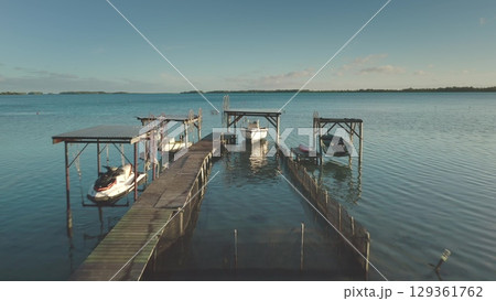 Wooden pier extending into turquoise lagoon, revealing shallow seabed, moored boats, and distant horizon under sunny skies, capturing tropical paradise landscape Wooden pier extending into turquoise lagoon, revealing shallow seabed, moored boats, and distant horizon under sunny skies, capturing tropical paradise landscape 129361762