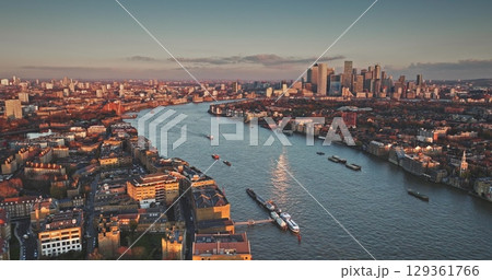 River Thames reflecting sunset warm light, flowing through London cityscape towards Canary Wharf, boats navigating, aerial view. United Kingdom, Europe. Travel destination. Drone flight River Thames reflecting sunset warm light, flowing through London cityscape towards Canary Wharf, boats navigating, aerial view. United Kingdom, Europe. Travel destination. Drone flight 129361766
