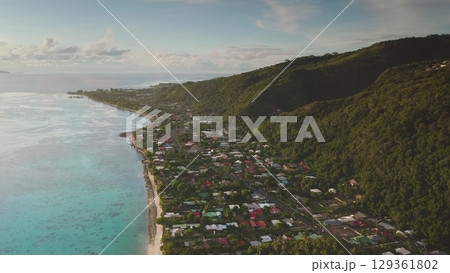 Aerial drone revealing Tahiti's vibrant coastline, where colorful houses blend with lush volcanic slopes, illuminated by the warm glow of sunset Aerial drone revealing Tahiti's vibrant coastline, where colorful houses blend with lush volcanic slopes, illuminated by the warm glow of sunset 129361802