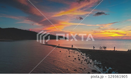 Tourists walking along the sandy stretch connecting Koh Ma to Koh Phangan, basking in the vibrant hues of a stunning sunset in Thailand's tropical paradise 129361905
