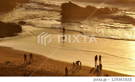 Lisbon, Portugal: Golden sunset casting a warm glow over the beach, with tourists walking along the shore, playing in the sand, and savoring the stunning scenery. Summer travel vacation background Lisbon, Portugal: Golden sunset casting a warm glow over the beach, with tourists walking along the shore, playing in the sand, and savoring the stunning scenery. Summer travel vacation background 129361928