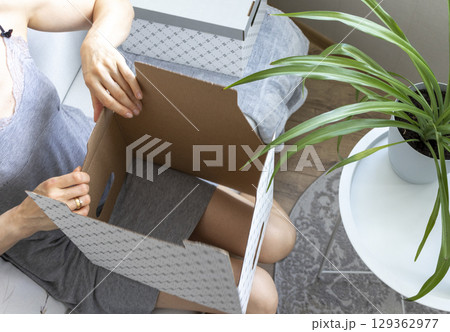 Woman sitting in the couch in cozy room, assembling carton box. Indoors 129362977