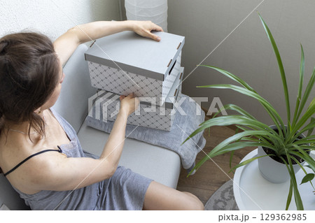 Woman sitting in the couch in cozy room, assembling carton box. Indoors 129362985