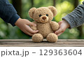 Tender hands holding light brown teddy bear outdoors 129363604