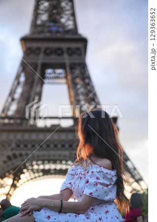 Woman in white floral dress sitting near Eiffel Tower in Paris at sunset 129363652