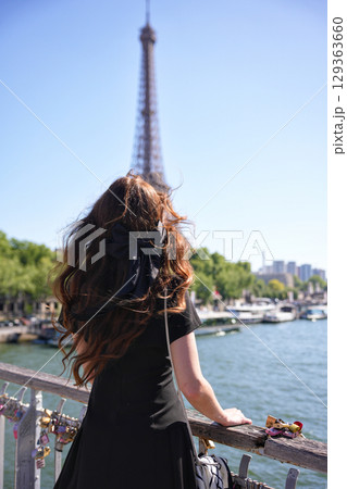 View of Eiffel Tower from bridge in Paris with woman standing by railing 129363660