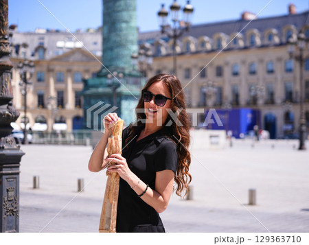 Smiling woman holding fresh baguette at Place Vendome Paris France on sunny day Smiling woman holding fresh baguette at Place Vendome Paris France on sunny day 129363710