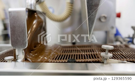 Chocolate production line depositing melted chocolate into molds Chocolate production line depositing melted chocolate into molds 129365590