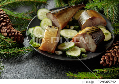 Smoked mackerel with fresh cucumber and green onions on a black plate. 129365742