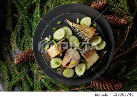 Smoked mackerel with fresh cucumber and green onions on a black plate. 129365746