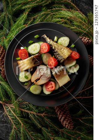 Smoked mackerel with fresh cucumbers, tomatoes and green onions on a black plate. Smoked mackerel with fresh cucumbers, tomatoes and green onions on a black plate. 129365747